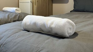 Un lit bien fait, avec une serviette blanche roulée, une armoire en bois, un radiateur et un miroir accroché au mur.
