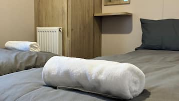Una cama bien hecha con una toalla blanca enrollada, un armario de madera, un radiador y un espejo en la pared.