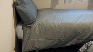 A small, single-bed room with a headboard, a window with floral curtains, and a carpeted floor.