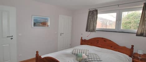 A bedroom with a wooden bed, a window with curtains, a door, and a wall-mounted light fixture.