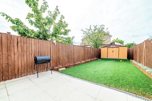 A backyard with a wooden fence, a barbecue grill, a shed, and a lawn. - Spacious 4BDR Home Garden and Parking in Windsor (Slough)