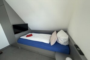 Ein kleines, modernes Zimmer mit einem Bett, einem Fernseher und einer Fernbedienung.