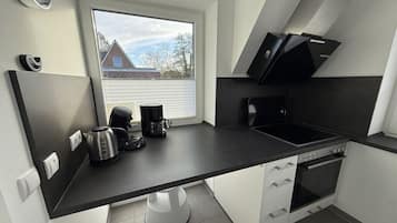 Een compacte keuken met een raam, een koffiezetapparaat, een waterkoker, een fornuis en een magnetron.