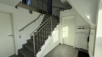 Een trap met metalen leuningen die naar een verdieping leidt, een witte deur en een radiator op de vloer.