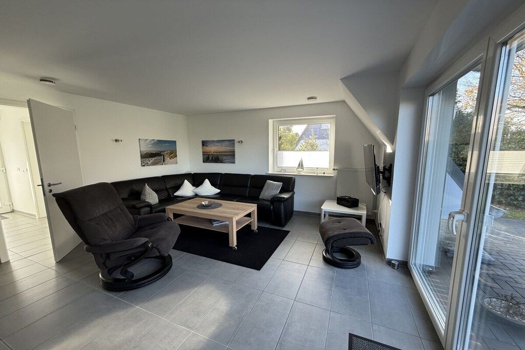 Een moderne woonkamer met een modulaire bank, een schommelstoel, een salontafel en een groot raam met uitzicht op de omgeving.