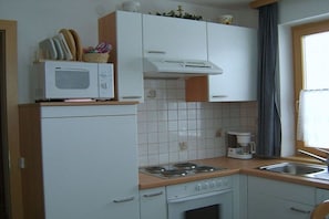 A compact kitchen with white cabinets, a microwave, a stove, and a coffee maker. - 2 Apartment House Bauer (Mariapfarr)