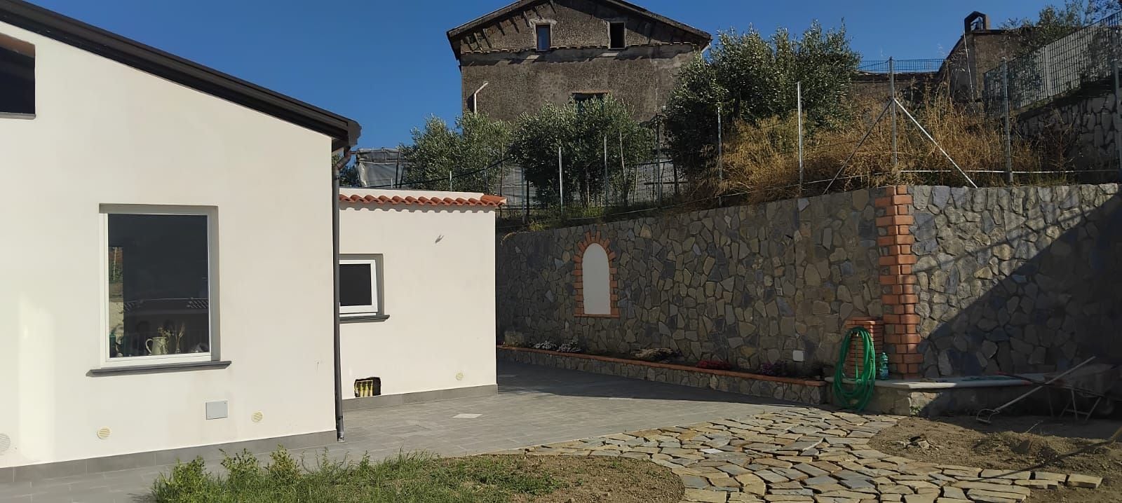 A courtyard with a white building, a stone wall, and a rustic tower in the background.