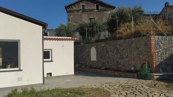 A courtyard with a white building, a stone wall, and a rustic tower in the background.