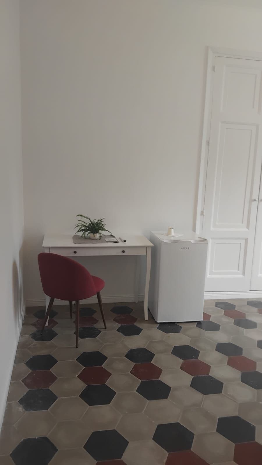 Ett rum med ett vitt skrivbord, en röd stol, en vit dörr och en vit papperskorg.