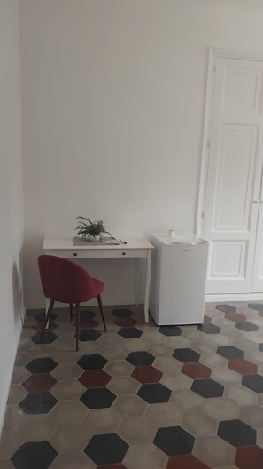 Una habitación con un escritorio blanco, una silla roja, una puerta blanca y un bote de basura blanco.