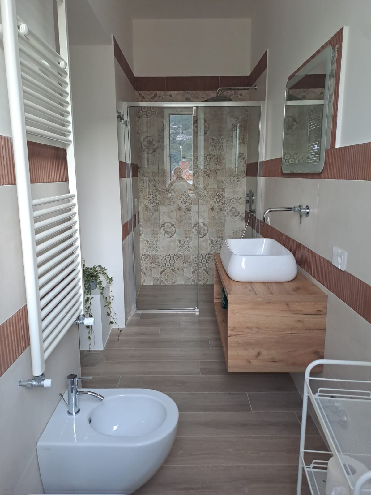 A modern bathroom with a bidet, two sinks, a mirror, and a shower area.