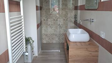 A modern bathroom with a bidet, two sinks, a mirror, and a shower area.