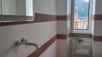 A bathroom with a large sink, a toilet, a mirror, and a window with a view of buildings and hills.