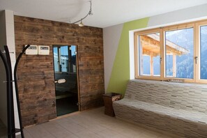 Una habitación con pared de madera, un banco, una ventana con vistas y una puerta que da a otra habitación.