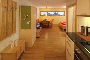 A compact kitchen with wooden cabinets, a dining area with a table and chairs, and a view of mountains through a window. - Holiday apartment with 1 bedroom (Damüls)