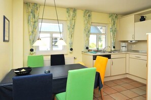 Eine kompakte Küche mit Esstisch, Stühlen und einem Fenster mit Vorhängen.
