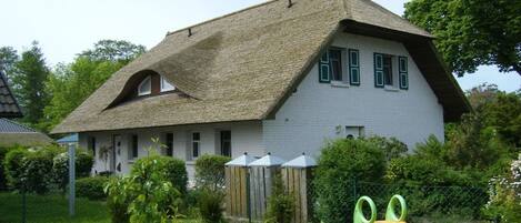 Une maison avec un toit à forte pente, un petit jardin avec un toboggan et un espace clôturé agrémenté d’une structure en bois.
