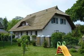 Ett hus med ett brant tak, en liten trädgård med en rutschkana och ett inhägnat område med en träkonstruktion.