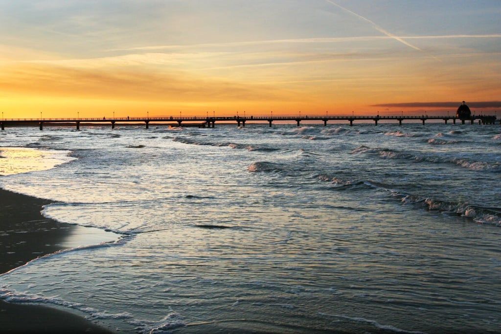 A coastal scene with a pier extending into the water, waves gently lapping at the shore, and a clear sky above.