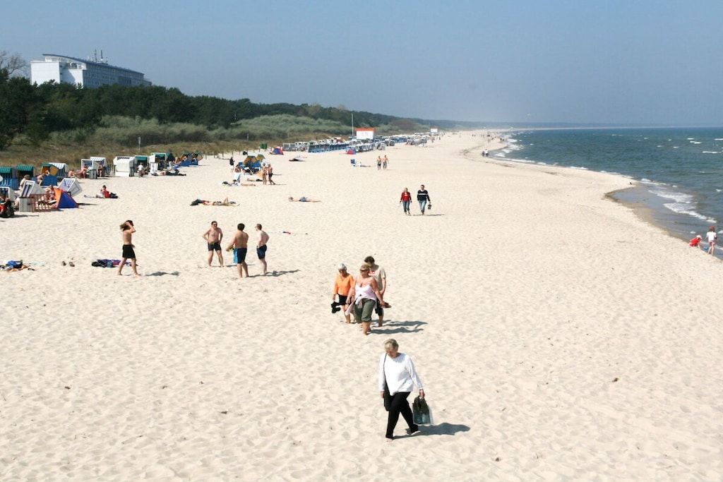 A beach with people walking and sunbathing, tents, and a building in the background.