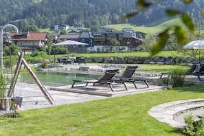 Ein Poolbereich mit Liegestühlen, einem Teich und Blick auf Häuser im Hintergrund.