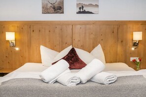 Ein Hotelzimmer mit einem Holzkopfteil, zwei Wandleuchten, einem Bett mit weißen Leinen, einem roten Kissen und einer kleinen Vase mit Blumen.