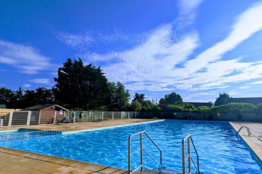 A swimming pool with a clear blue sky, surrounded by a fence and trees.