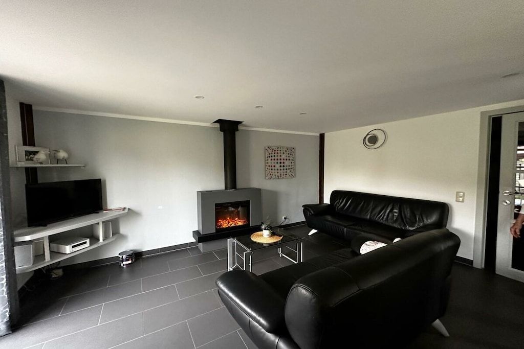 A modern living room with a fireplace, a black leather sofa, and a television on a white stand.