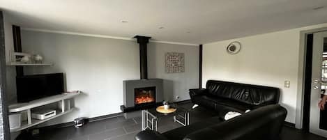 A modern living room with a fireplace, a black leather sofa, and a television on a white stand.