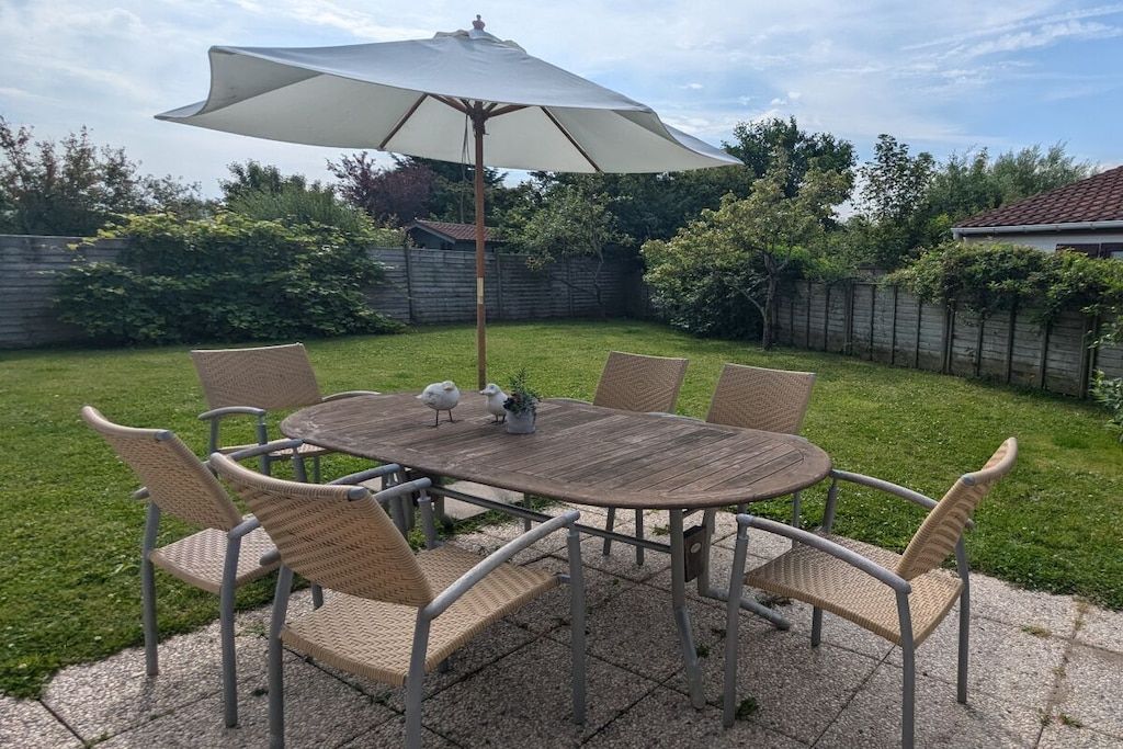 A round wooden table with six wicker chairs and a large umbrella.