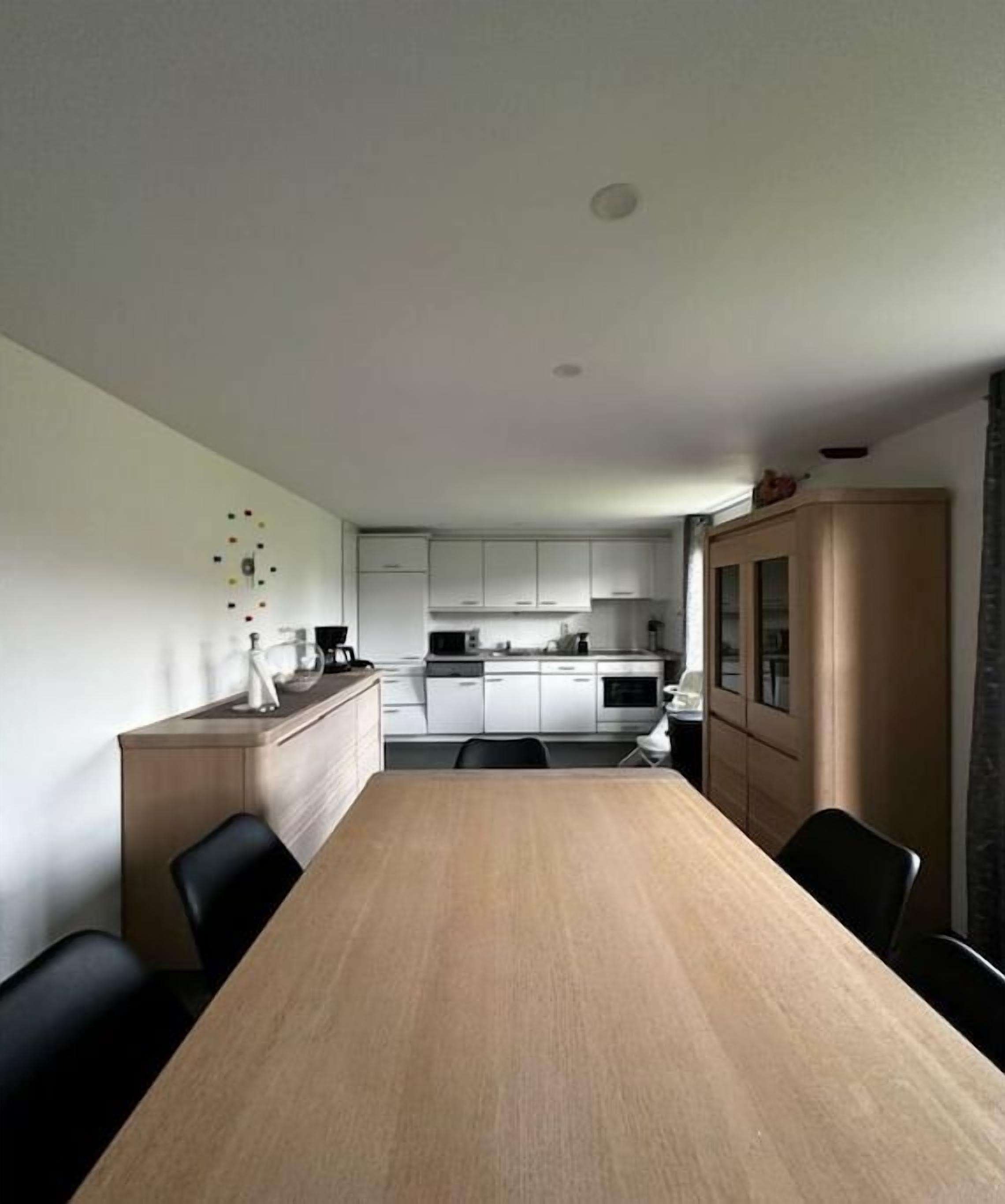 Une cuisine moderne avec des meubles blancs, une table à manger en bois et des chaises noires.