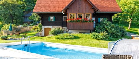 Ett trähus med ett rött tak, en swimmingpool och utemöbler.