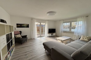 A living room with a sofa, TV, and a bookshelf. - Holiday apartment with 2 bedrooms (Hagermarsch\/OT Hilgenriedersiel)