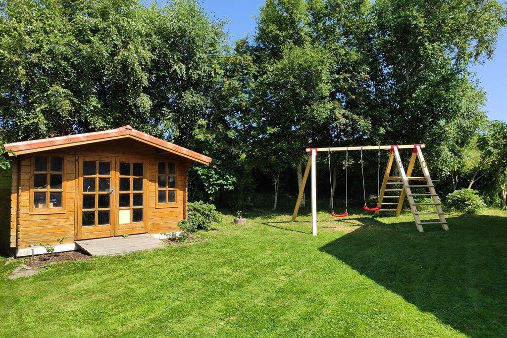A wooden cabin with a porch and a swing set in a grassy backyard.