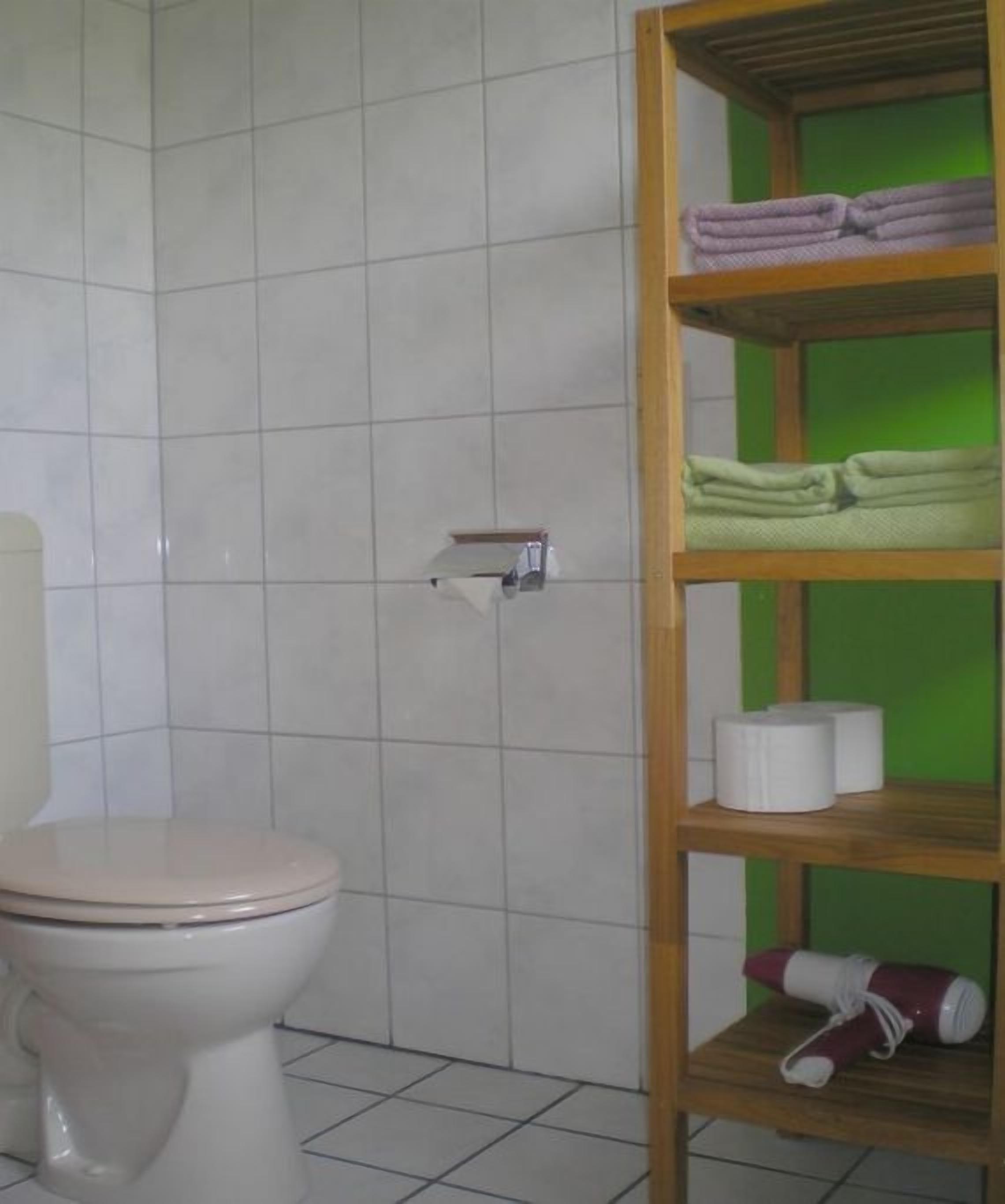 A bathroom with a toilet, a shelf with folded towels, toilet paper, and a water bottle.