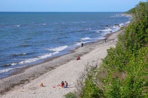 Ein Strand mit felsigem Ufer, Menschen die entlanggehen, und einem klaren Himmel.