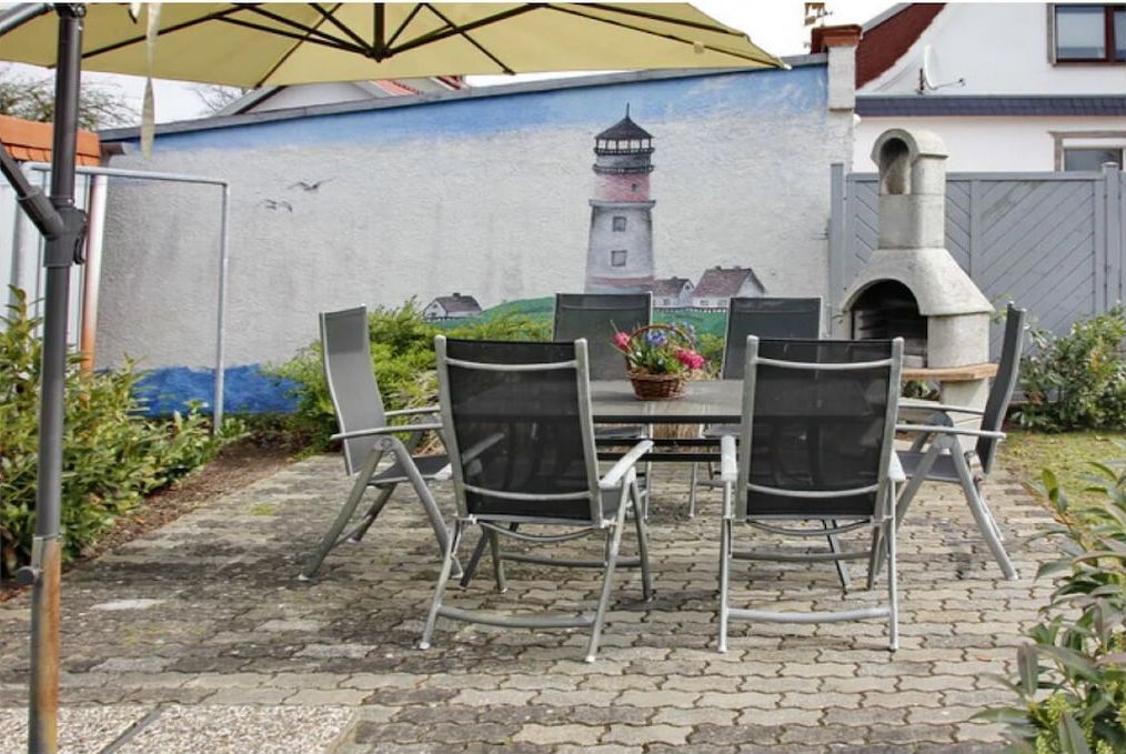Een terras buiten met een tafel, stoelen, een muurschildering van een vuurtoren en een stenen oven.