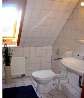 Ein kleines Badezimmer mit Fliesen, Toilette, Waschbecken und Heizkörper.