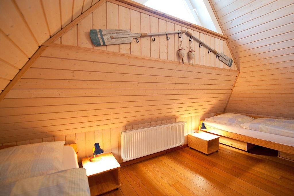 A small, sloped-roofed room with a wooden floor, a bed, a radiator, and a wall-mounted broom.