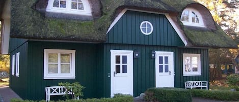 A traditional house with a thatched roof, white-framed windows, and a green exterior.