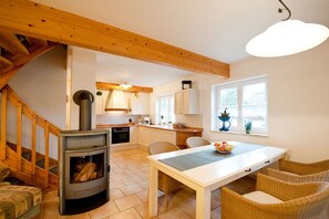 A cozy kitchen with a wood-burning stove, a dining table with chairs, and a staircase. - Haus Wels in Born a. Darss (Born a. Darß)