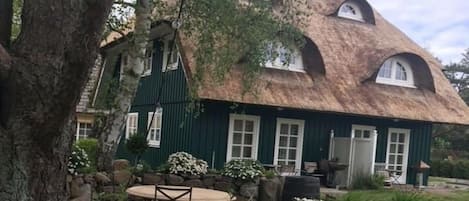 A thatched-roof house with a stone patio, a table, and chairs.
