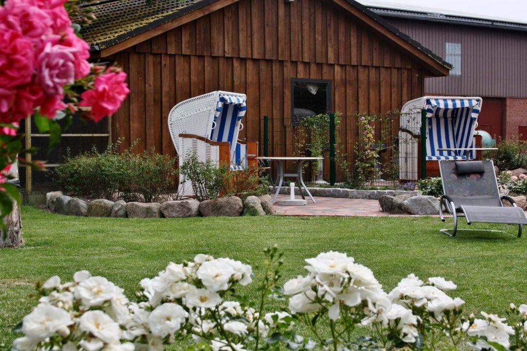 A wooden barn with two outdoor seating areas, one with striped chairs and the other with a single lounge chair.