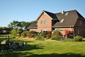 A two-story brick house with a sloped roof, a front porch, and a well-maintained lawn. - Holiday apartment with 3 bedrooms (Fehmarn)
