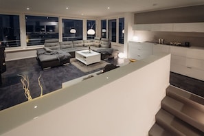 A modern living room with a sectional sofa, a coffee table, and a dining area with a kitchen in the background. - Holiday home with 2 bedrooms (Bitterfeld)