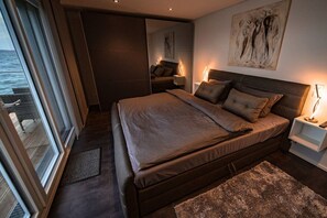 A bedroom with a large bed, a nightstand, a wall-mounted artwork, and a view through a window. - Holiday home with 2 bedrooms (Bitterfeld)
