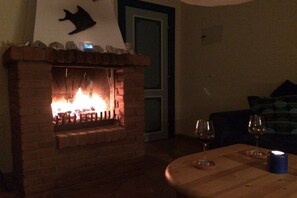 Ein Kamin aus Ziegelsteinen mit brennendem Feuer, ein Tisch mit Weingläsern und ein Sofa in einem schwach beleuchteten Raum.