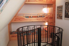 Ein Stockbett mit Holzrahmen und schwarzer Metallreling steht in einem Zimmer mit weißer Wand und einem Poster.