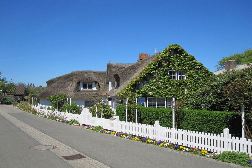 A row of houses with thatched roofs, white picket fences, and flower beds.