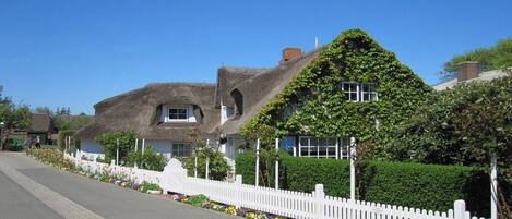 A row of houses with thatched roofs, white picket fences, and flower beds.